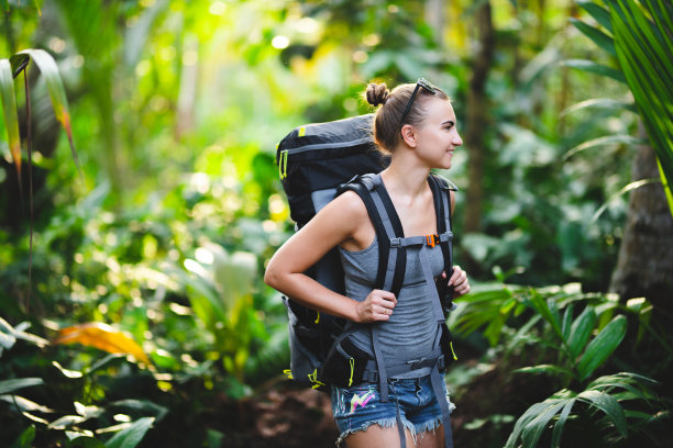 苗条的年轻女孩背着徒步旅行背包在丛林里。白种白人女孩在丛林里徒步旅行。图片下载