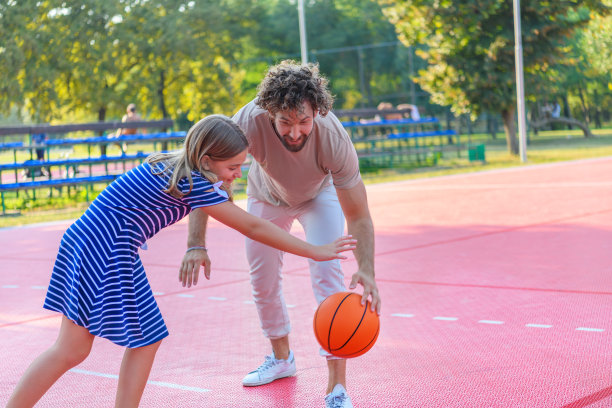年轻的父亲和他可爱的女儿在公园里玩篮球。图片下载