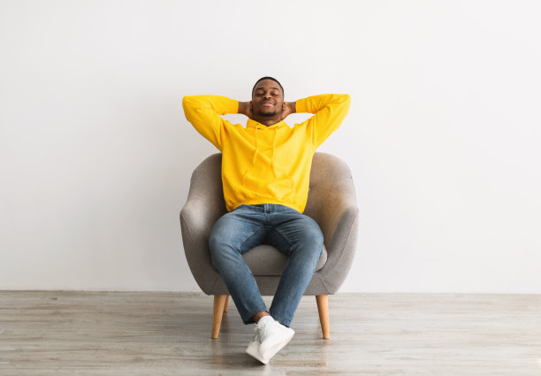 放松的黑人男子坐在椅子上休息在灰色的背景图片下载