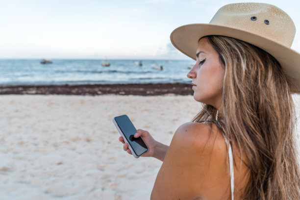 戴着帽子的年轻女子在海滩上使用手机图片下载