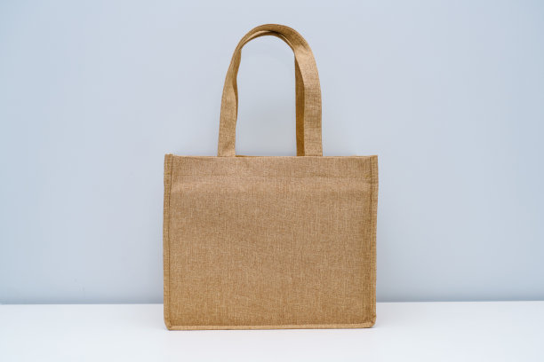 白色的桌子上放着一个卡其色的棉麻手提袋。图片下载