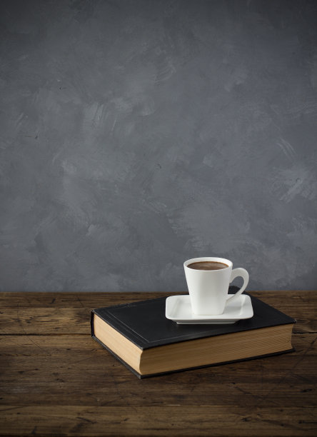白色的咖啡杯放在一本古书上，棕色的木桌，灰色的混凝土背景墙，靠得很近图片下载