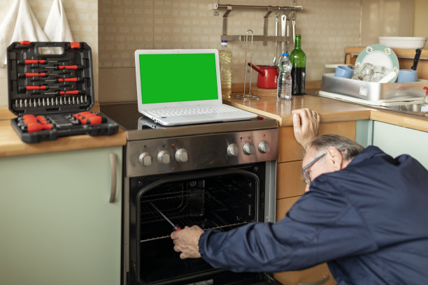 一位老人正在厨房里修烤箱。图片下载