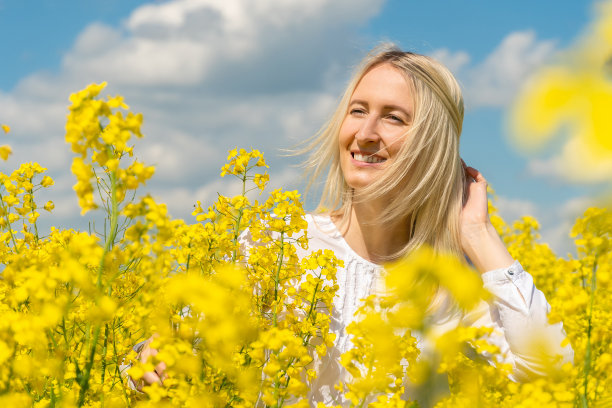一个美丽的快乐的年轻金发女人的肖像在一个阳光明媚的日子里一件白色的衬衫在油菜田图片下载