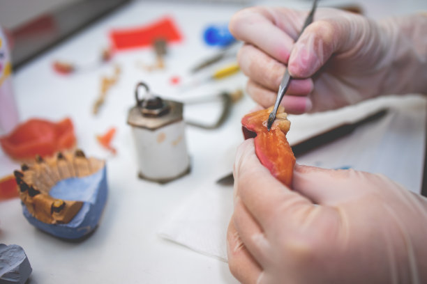 一个牙科技术人员塑造一个修复牙齿的工具在工作桌上的特写。图片下载