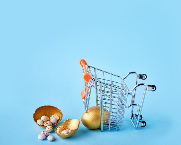 复活节销售的概念。金色的复活节彩蛋从小购物车上掉下来，摔碎在蓝色的背景上图片下载
