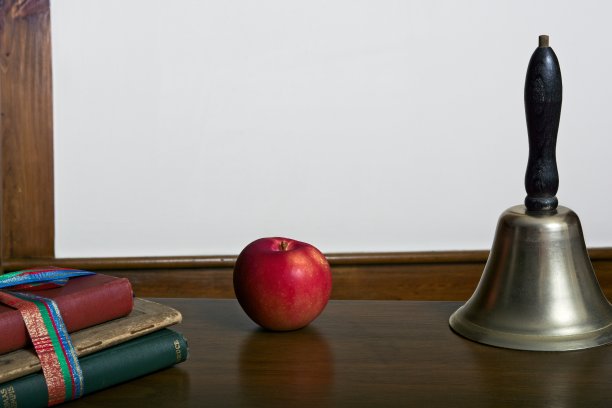 在白色的抄本空间前，有教科书、苹果和手铃的古董课桌概念图片下载