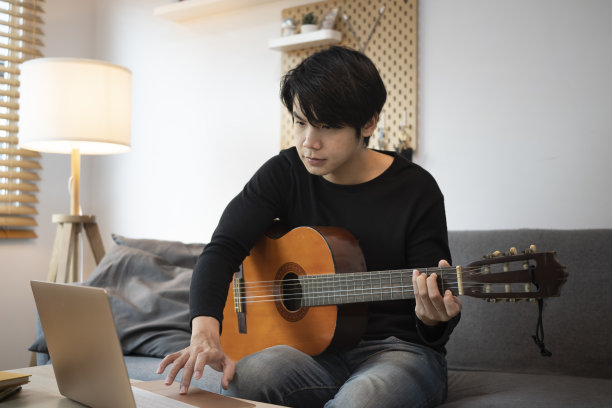 年轻人在客厅里用笔记本电脑弹吉他。图片下载