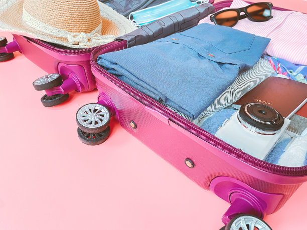 粉色背景上有衣服和面具的旅行袋。新冠肺炎疫情下的暑期旅游。图片下载