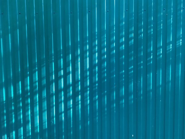 蓝色抽象背景的波纹金属栅栏在阳光下有平行和交叉的阴影图片下载