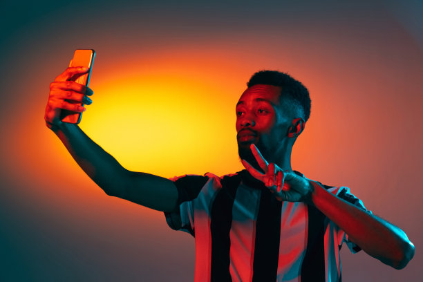非洲青年与手机孤立在彩色工作室背景霓虹灯。人类情感的概念，面部表情。图片下载