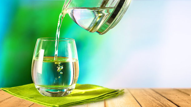 将罐子里的纯净水倒进木桌上绿色餐巾上的玻璃杯里。图片下载