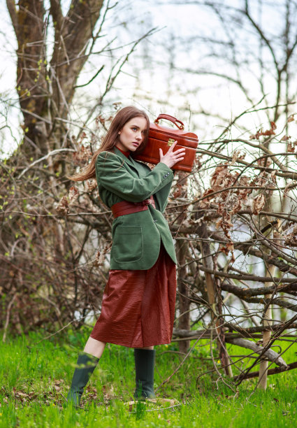 时尚的年轻女士在时尚的乡村服装与手提箱在森林图片下载
