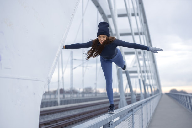 年轻快乐的健身妇女在冬天蓝色运动服做身体平衡在桥栅栏在寒冷的一天图片下载