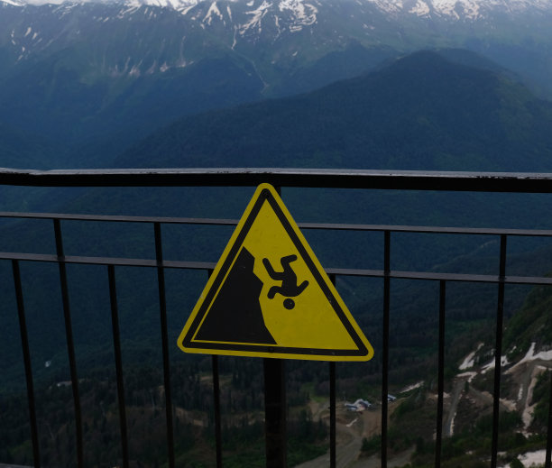 山上有黄色危险标志。山上有从悬崖边上掉下来的警告信号。有坠落的危险。徒步旅行安全警告。危险坠落，悬崖边缘的警告信号。图片下载