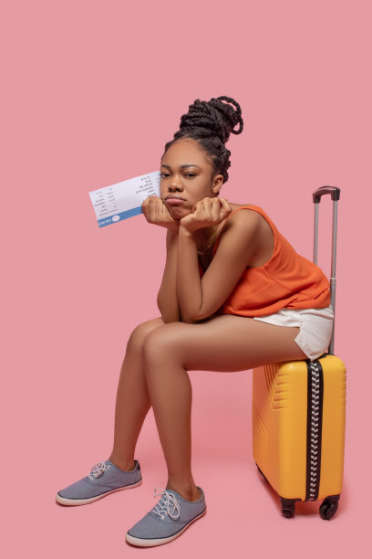 深色皮肤的女人拿着一个手提箱和一张机票，看起来很期待图片下载