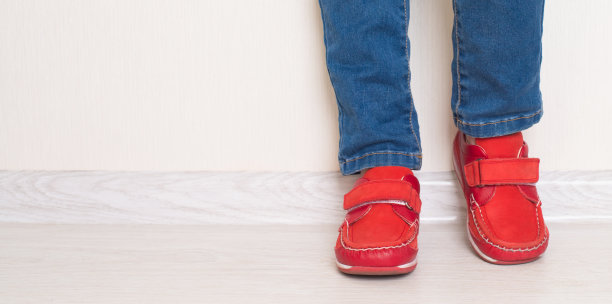 孩子摆着她的牛仔裤和红鞋站在白墙附近。图片下载