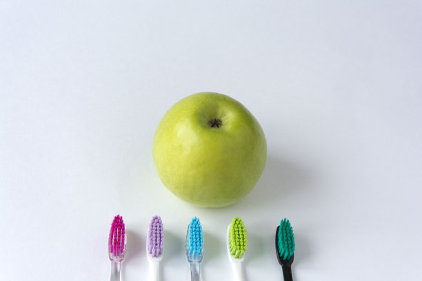 一个绿色多汁的苹果，旁边有几把彩色的牙刷，背景是白色的图片下载