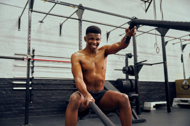 年轻的非洲裔美国男性在健身房锻炼。上身赤裸的男性私人教练使用绳子加强他的手臂。高质量的照片图片下载