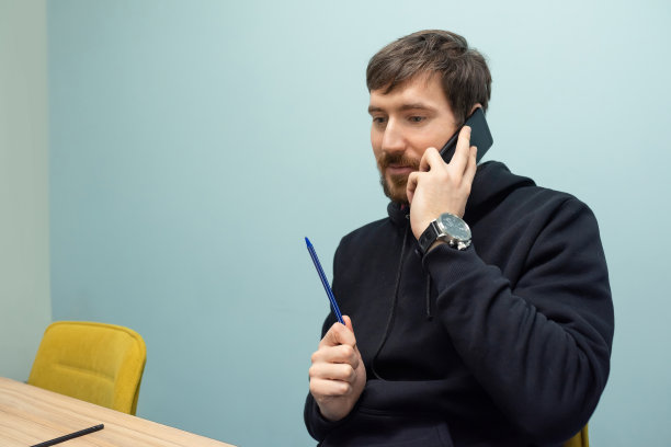 一个年轻人坐在他的桌子旁打电话。商业、在线培训、合作图片下载