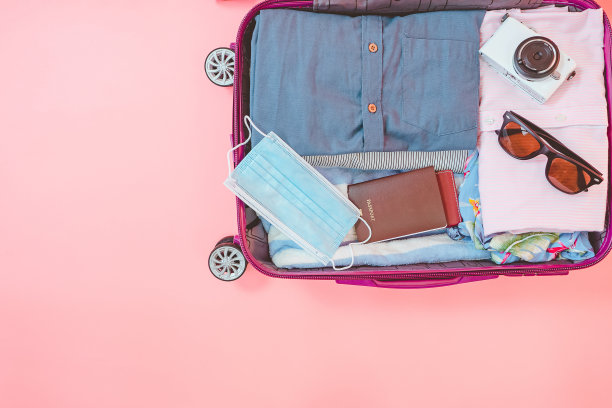 粉色背景上有衣服和面具的旅行袋。新冠肺炎疫情下的暑期旅游。图片下载