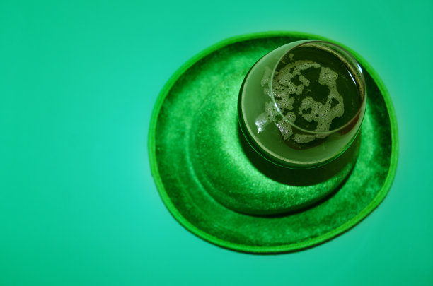 圣帕特里克节快乐。一杯绿色啤酒。派对眼镜和帽子在绿色背景。贺卡。副本的空间。前视图。图片下载