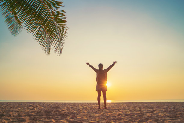 在海滩和棕榈树的背景下，复制日落天空上女人举手的空间。图片下载