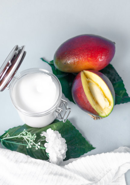 这是一个芒果身体霜的罐子，在灰色的背景上有两片芒果片和两片人造的植物叶子图片下载
