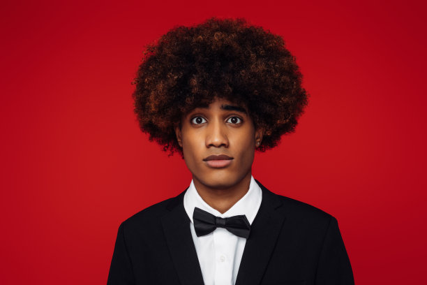 非洲裔美国人，头发是非洲式的，穿着燕尾服，站在孤立的红色背景上图片下载