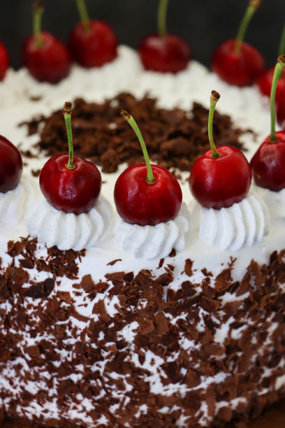 黑色森林蛋糕的图片，上面是圆形的奶油玫瑰，上面是羊奶樱桃，豪华的巧克力蛋糕上有奶油霜，蛋糕架上覆盖着巧克力刨花，黑色的背景，高视点，关注前景图片下载
