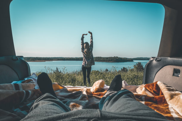 宁静美丽的景色，一个苗条的年轻女子做热身的背景自然湖，森林从一辆汽车在一个露营，人的腿在前景在一个夏天阳光明媚的一天。彩色照片图片下载