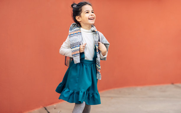 快乐的学龄前儿童去学校，在橙色背景下摆姿势。漂亮的小女孩背着背包在户外散步。图片下载