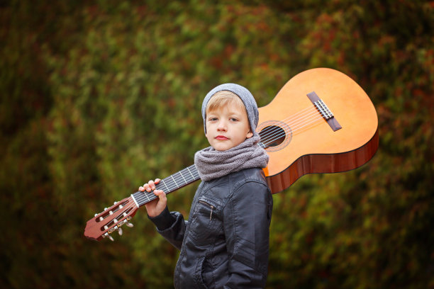 可爱的小男孩与吉他在自然背景。他是穿着图片下载