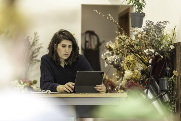 一个开朗的年轻女子在花店工作，在一台小笔记本电脑前安排会议议程，女商人的概念。图片下载