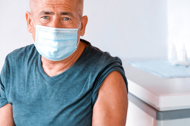 戴着防护面具准备注射的老人。医院门诊部主任老年人接种疫苗。成人COVID - 19冠状病毒疫苗。老年患者的保护。图片下载