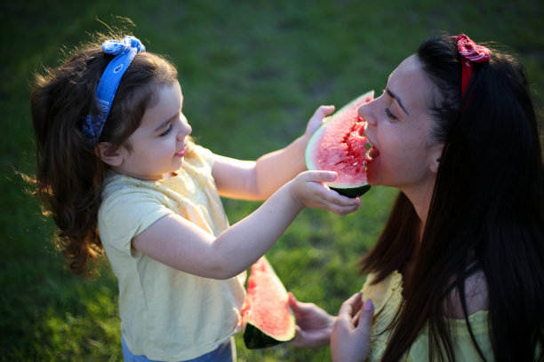 可爱的女儿和妈妈在夏天吃西瓜。公园里的快乐女孩。库存图片图片下载