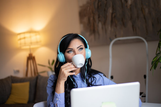 年轻女子享受她的咖啡，而工作或学习笔记本电脑在家庭办公室库存照片图片下载