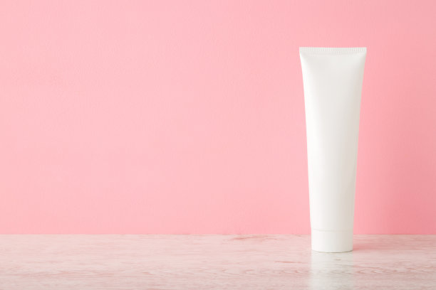 木桌上的白色塑料管，浅粉色的墙面背景。柔和的颜色。关心脸、手、腿和身体皮肤。美容产品。特写镜头。文字或标识的空白位置。前视图。图片下载