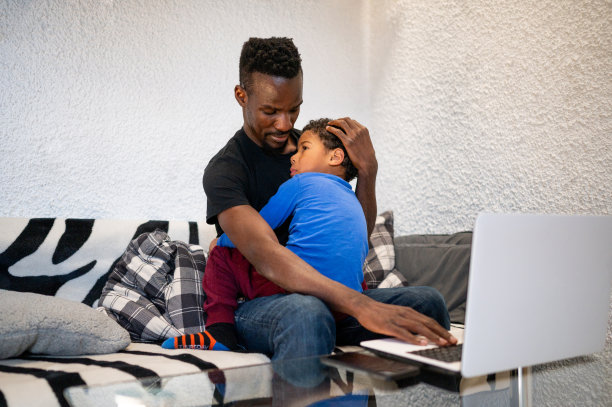 一位单身父亲在家工作时安慰坐在他腿上的儿子图片下载