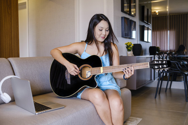 亚洲妇女的肖像享受一个放松的时刻在家里弹吉他。图片下载