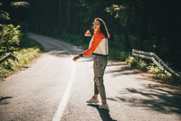 一个年轻女子走在森林里的路中间，从肩膀上看镜头图片下载