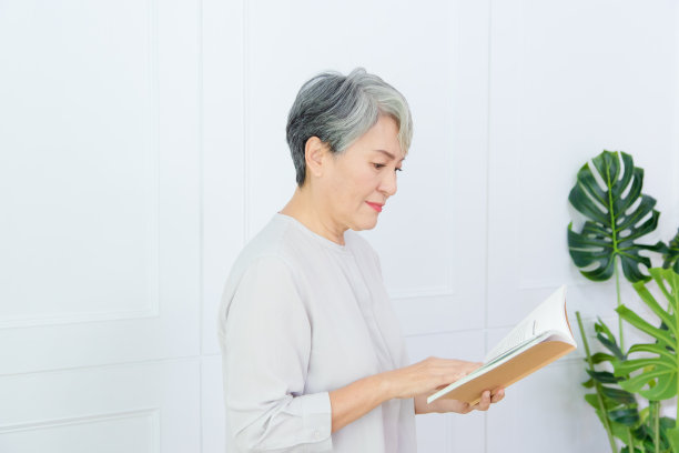 资深亚洲妇女正在阅读白色背景的书。图片下载