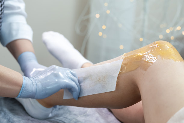 女性保健的概念。美容师做脱毛与热蜡在女人的腿上使用液体蜡在水疗。水平图像组成图片下载