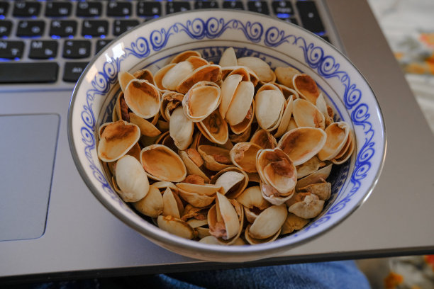 一碗开心果皮在蓝色盘子特写俯视图上的笔记本电脑。快餐食品。图片下载