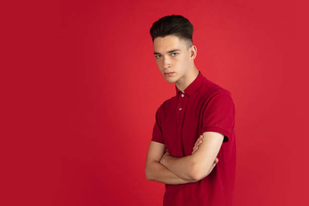 一个年轻的白人男孩被隔离在红色的工作室背景下。面部表情，人类情感的概念。图片下载