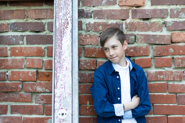 一个穿着时髦的男人，穿着一件蓝色的衬衫，站在一扇破旧的门旁边，靠砖墙。特写镜头。有选择性的重点图片下载