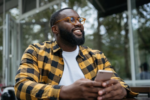 微笑英俊的非裔美国人用手机，网上购物。照片上的年轻人戴着时髦的眼镜，拿着智能手机，聊天，在线交流，坐在户外图片下载