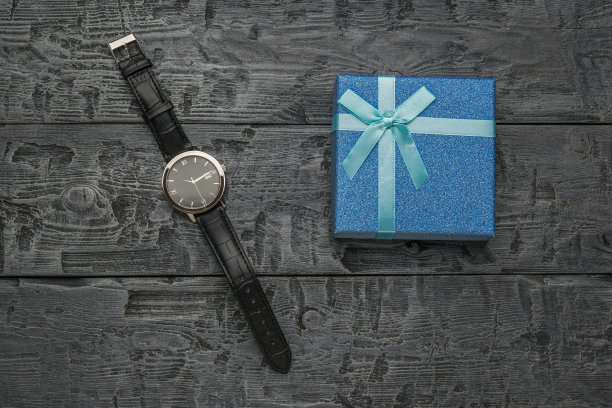 黑色木桌上有一只带指针的男表和一个礼盒。图片下载