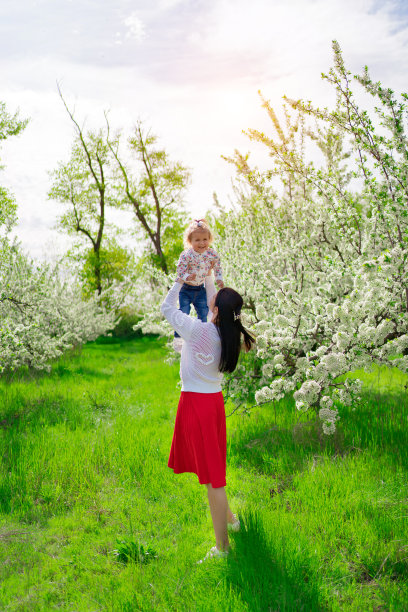 妈妈把女儿扔在公园里一棵开花的树旁。图片下载