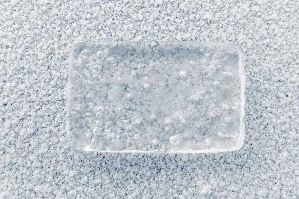 这是一块长方形的纯净透明的冰，上面有气泡，表面是白色的雪。纯洁的概念。图片下载